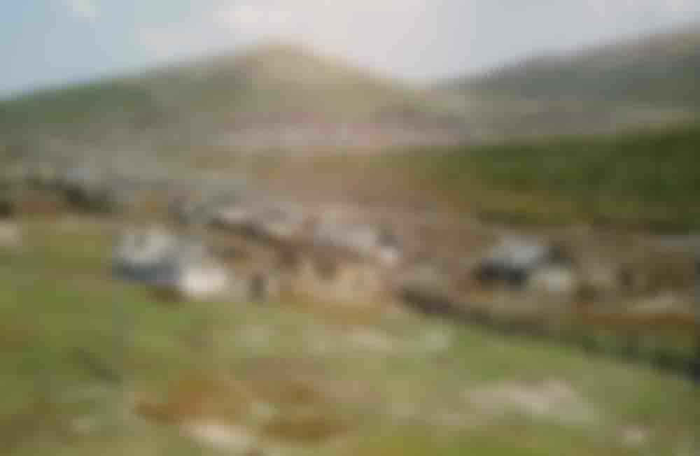Wooden homes dot the landscape. Village seen from the train, location unknown.